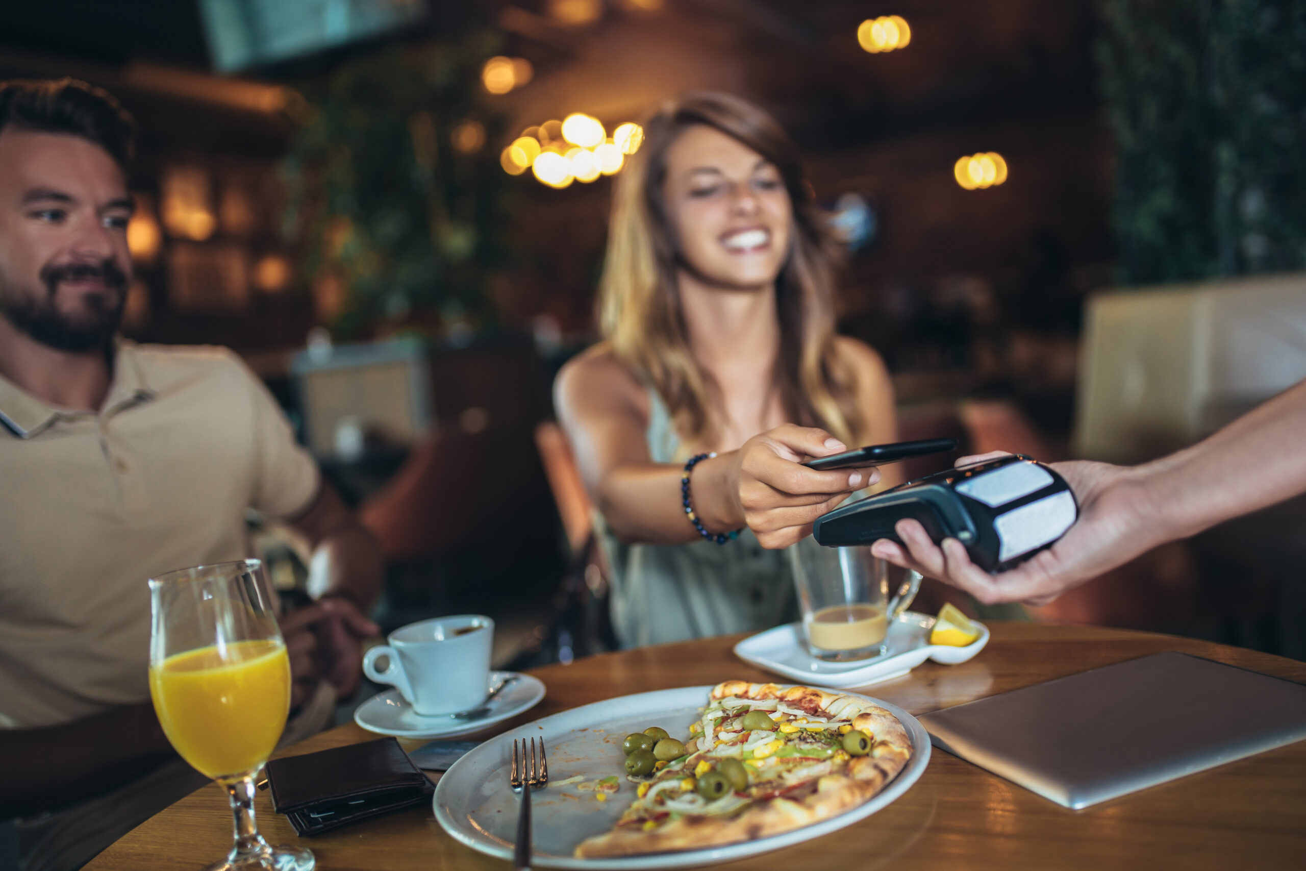 Happy couple using mobile phone and making contactless payment in a restaurant. Selective focus.